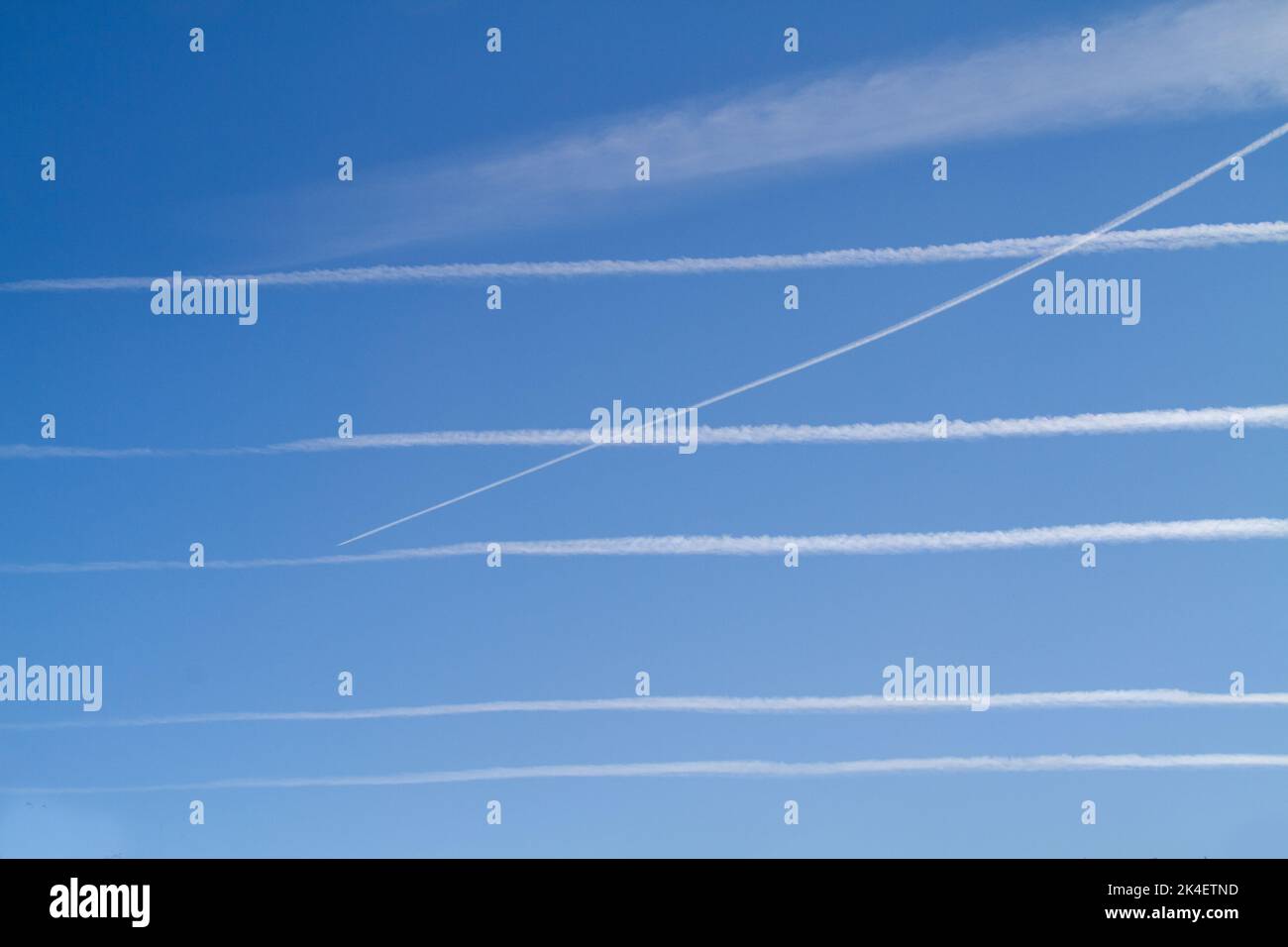 Six condensation trails, contrails or vapor trails in a blue sky, five parallel and horizontal and one crossing them Stock Photo