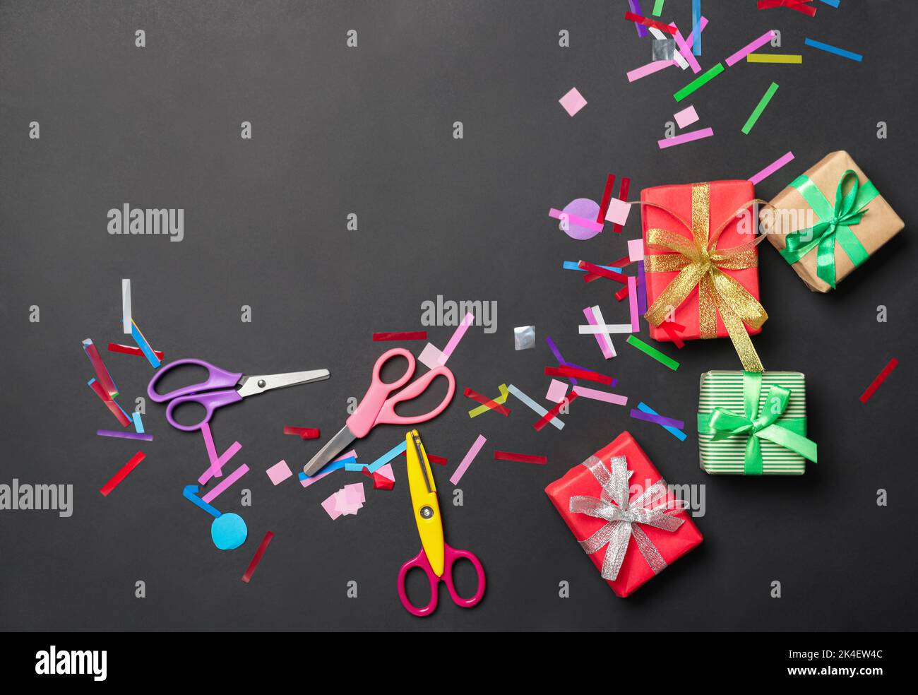 Scissors with gift boxes and confetti on black background Stock Photo