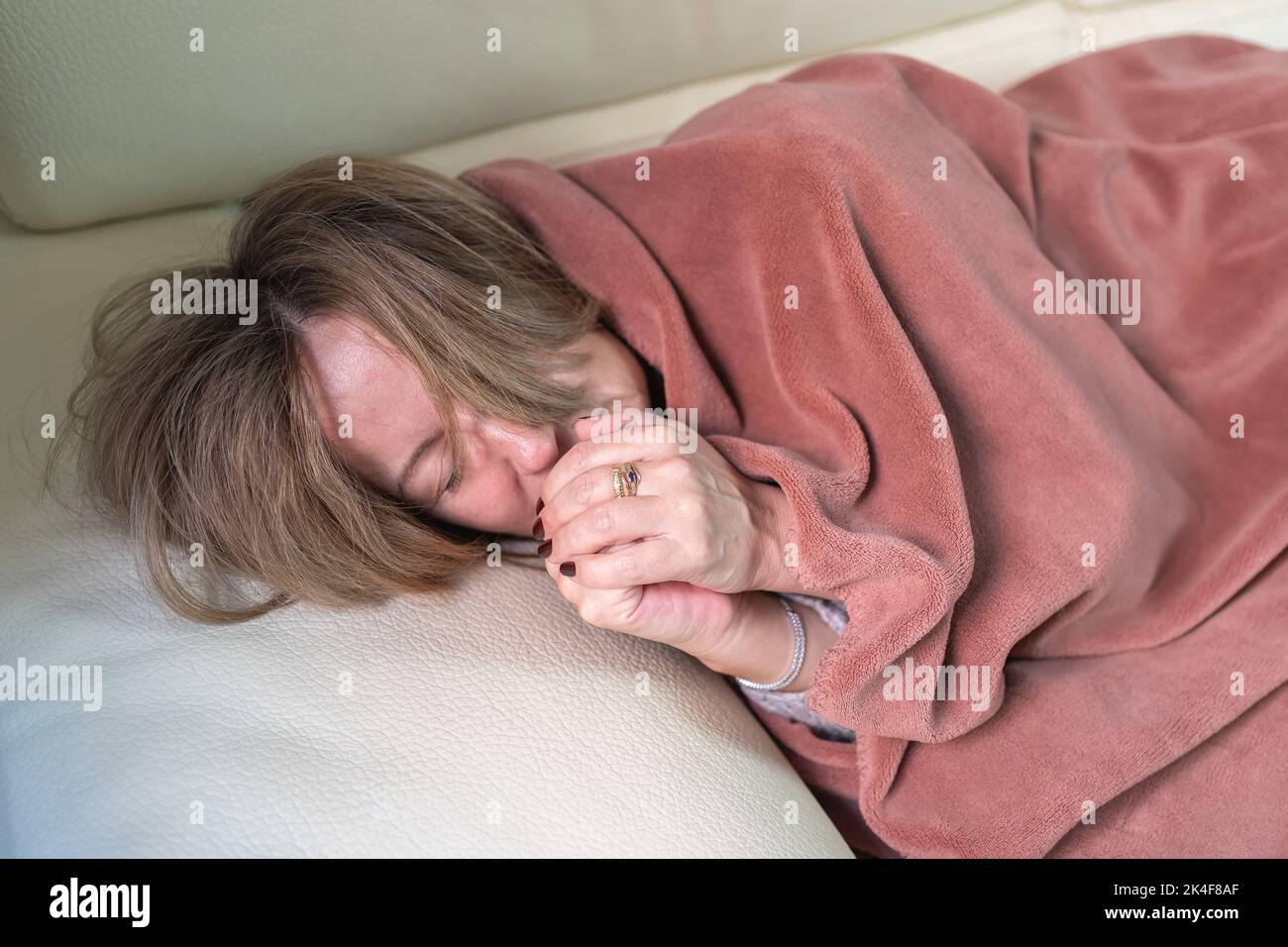 Woman lying on a sofa and going cold through the winter and energy saving, blowing her hands to warm herself. Stock Photo