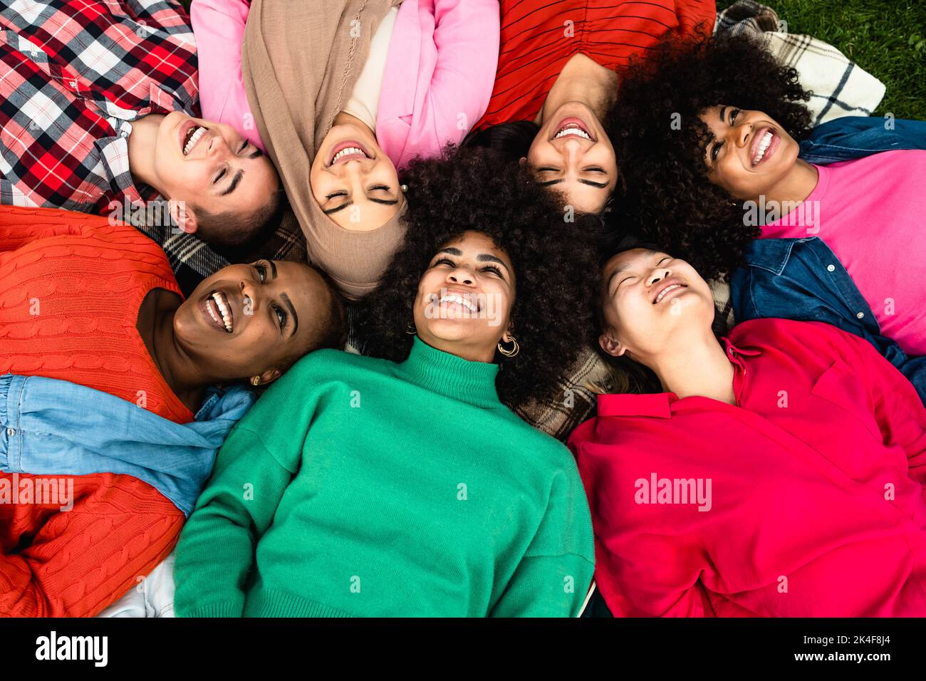 Happy young multi ethnic women having fun lying on park grass - Diversity and friendship concept Stock Photo