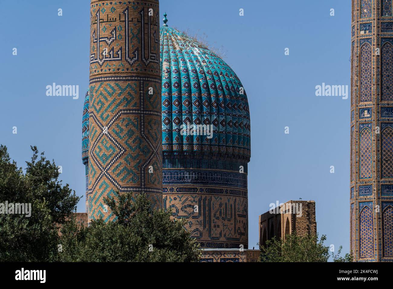Zoom of Blue tile minaret dome and wall of Bibi-Khanym Mosque in bright blue sky in Samarkand. Stock Photo