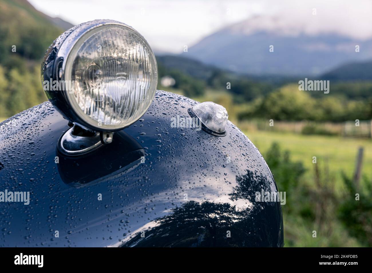 Reflections and raindrops on the paintwork of the mudguard, bodywork and headlamp of a Citroen Light 15 vintage car in the Lake District, Cumbria, Eng Stock Photo