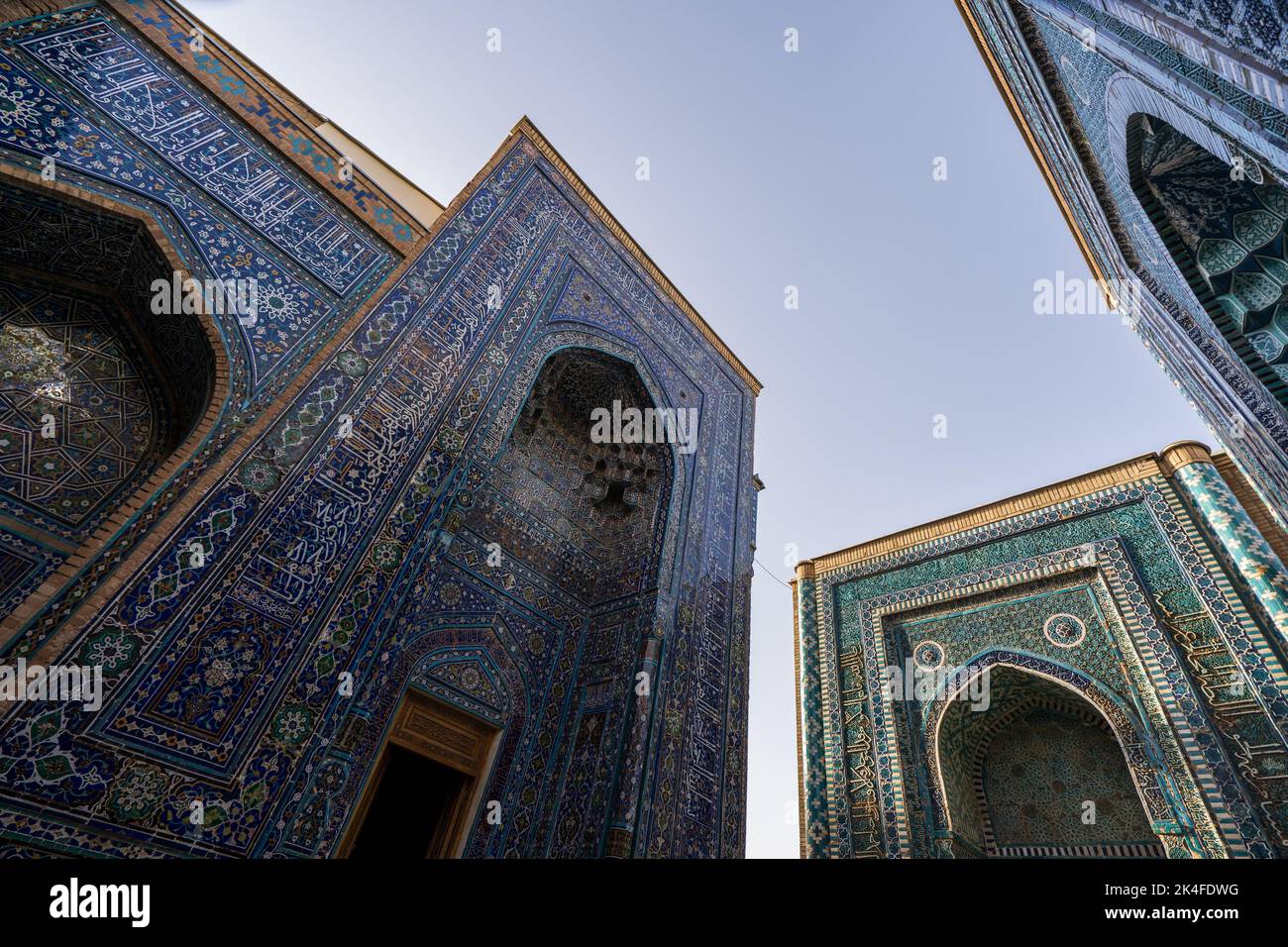 Looking up at the blue tiled facades and arches of the Shah-i-Zinda mausoleum complex at sunset, Samarkand Stock Photo