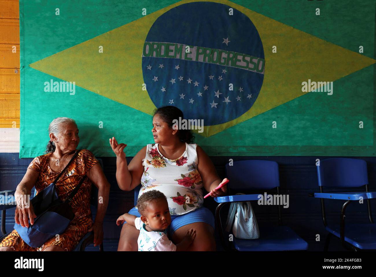 Women sit underneath the Brazilian flag while waiting to cast their votes at a polling station set up on a floating school on the Negro river, in the Catalao Community, Brazil October 2, 2022. REUTERS/Bruno Kelly Stock Photo