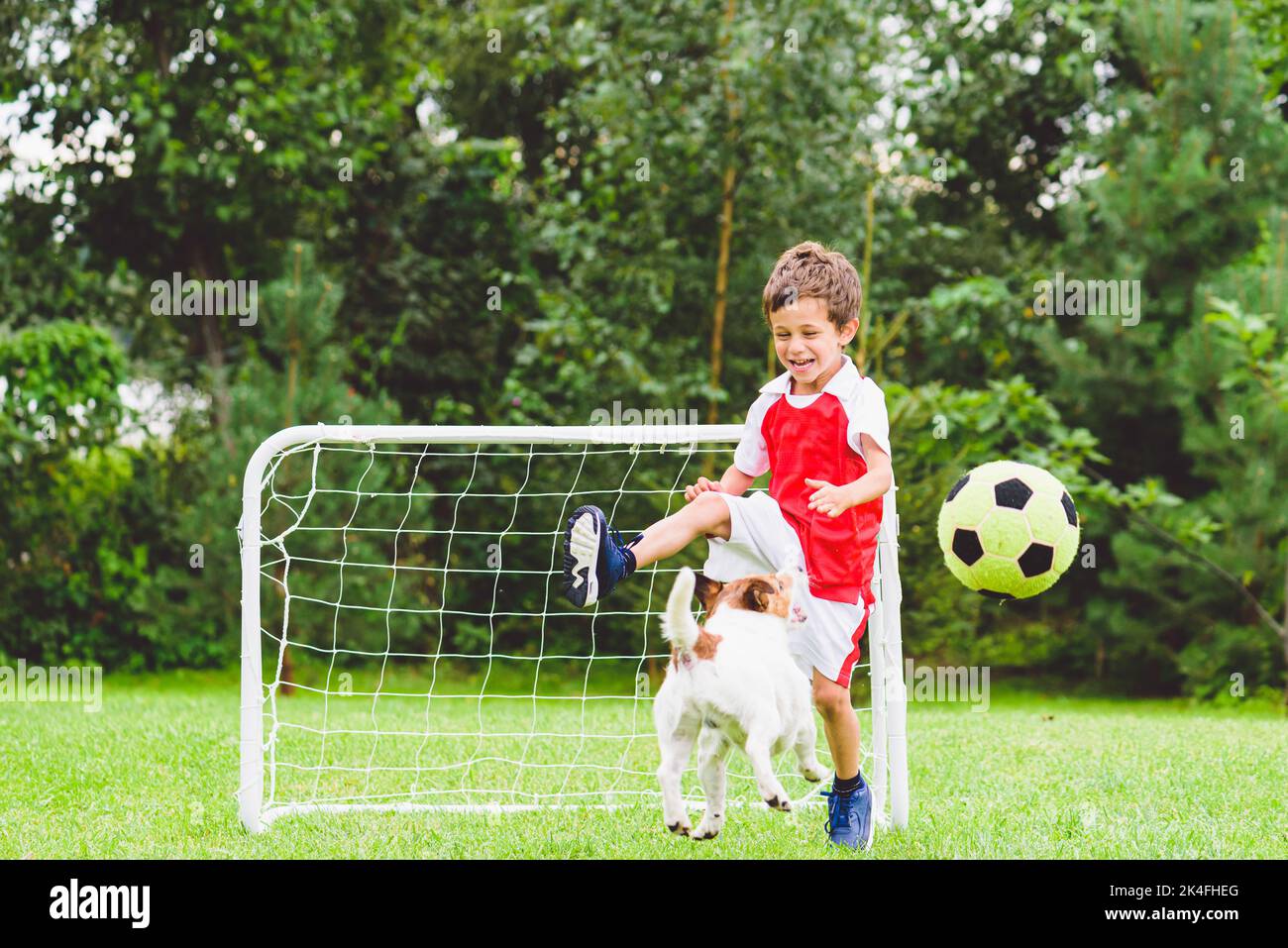 Excited child playing football (soccer) kicks ball while his dog
