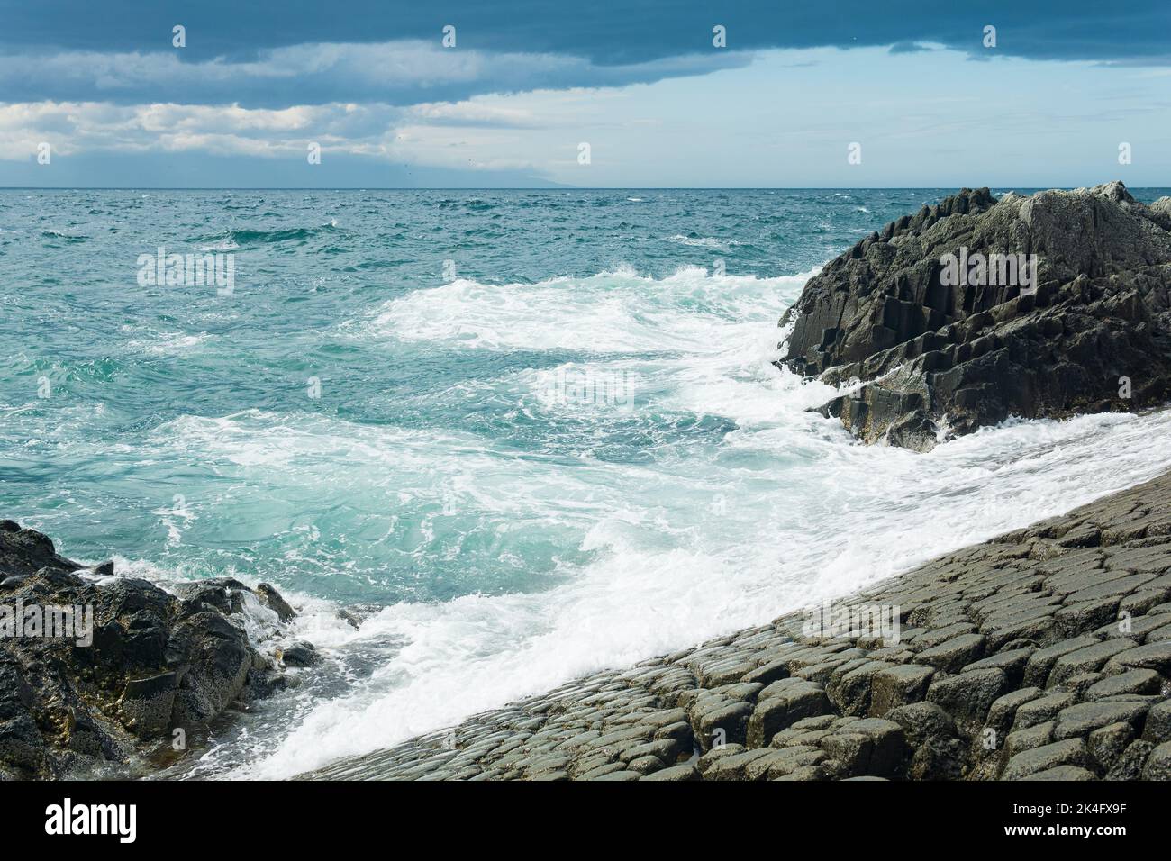 rocky seashore formed by columnar basalt against the surf, coastal landscape of the Kuril Islands Stock Photo