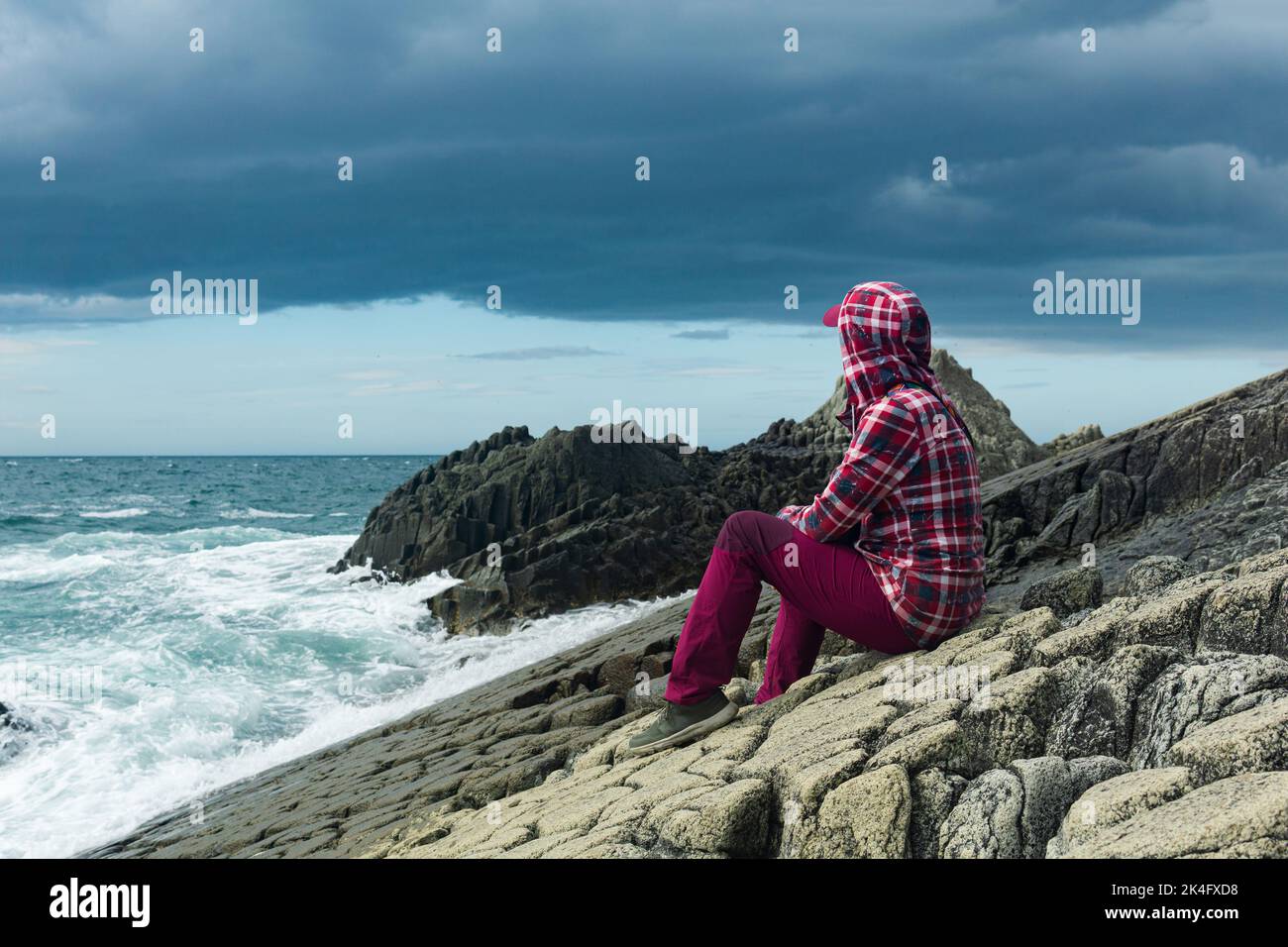 traveler sits on the shore of a stormy sea, on a natural pavement made of columnar granite Stock Photo