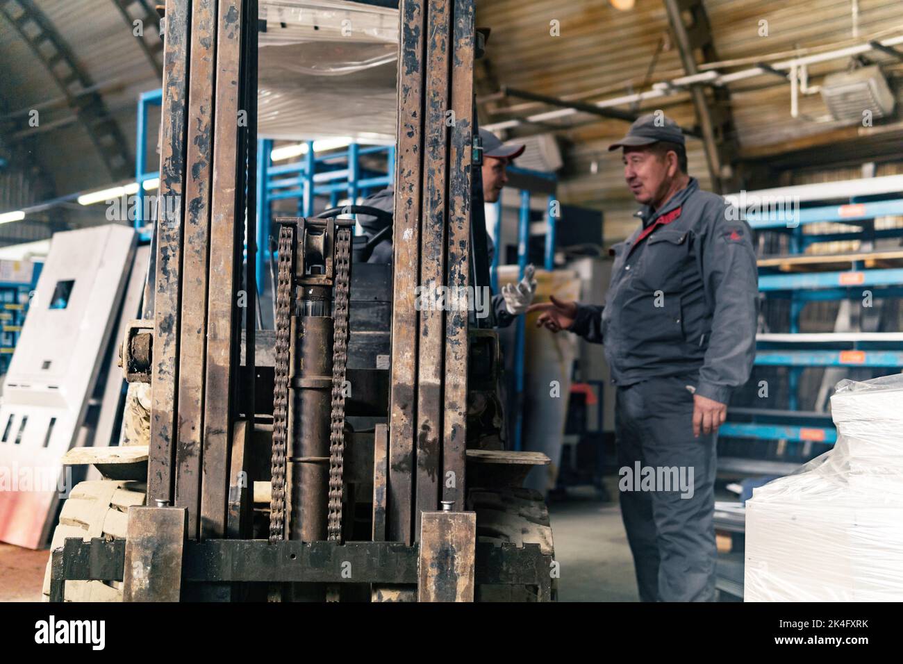 Perm, Russia - September 21, 2022: forklift driver and worker in an industrial warehouse, in the foreground the mechanism of the loader Stock Photo