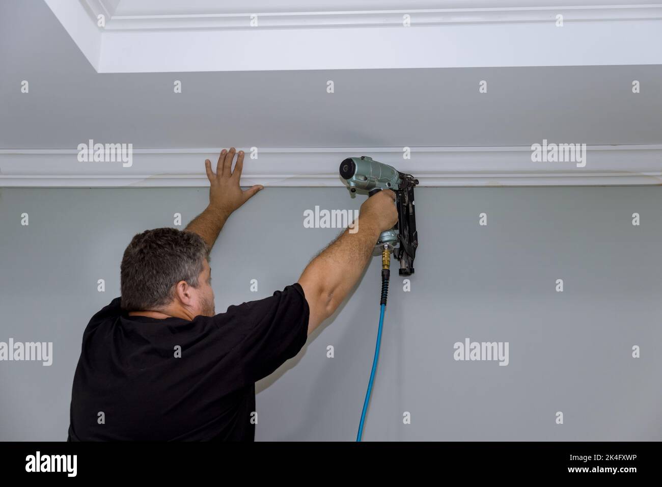As this professional carpenter nails wooden crown molding between the