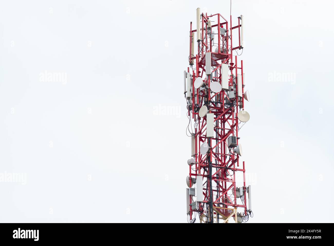 upper part of the radio tower with installed antennas and other equipment against a white cloudy sky Stock Photo