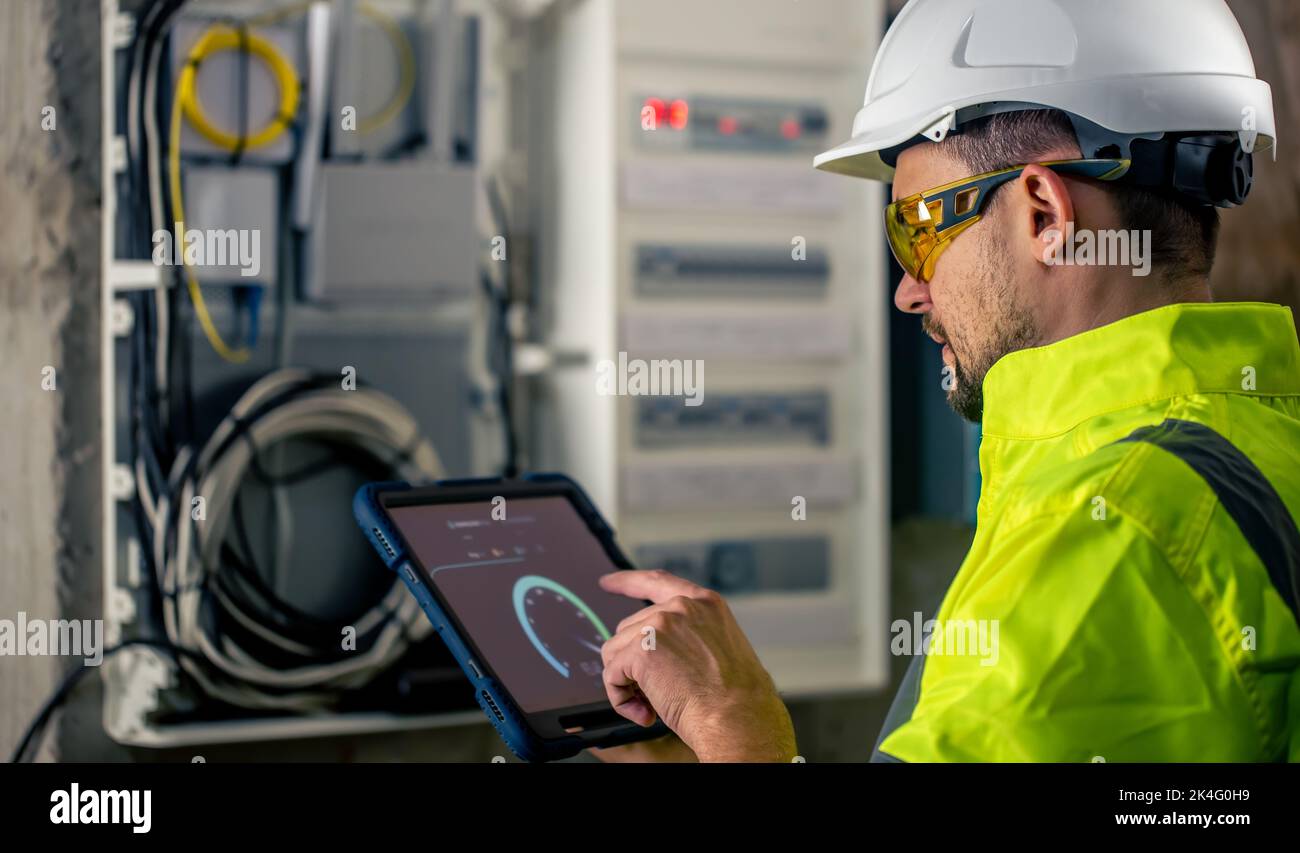 Man an electrical technician working in a switchboard with fuses, uses a tablet. Stock Photo