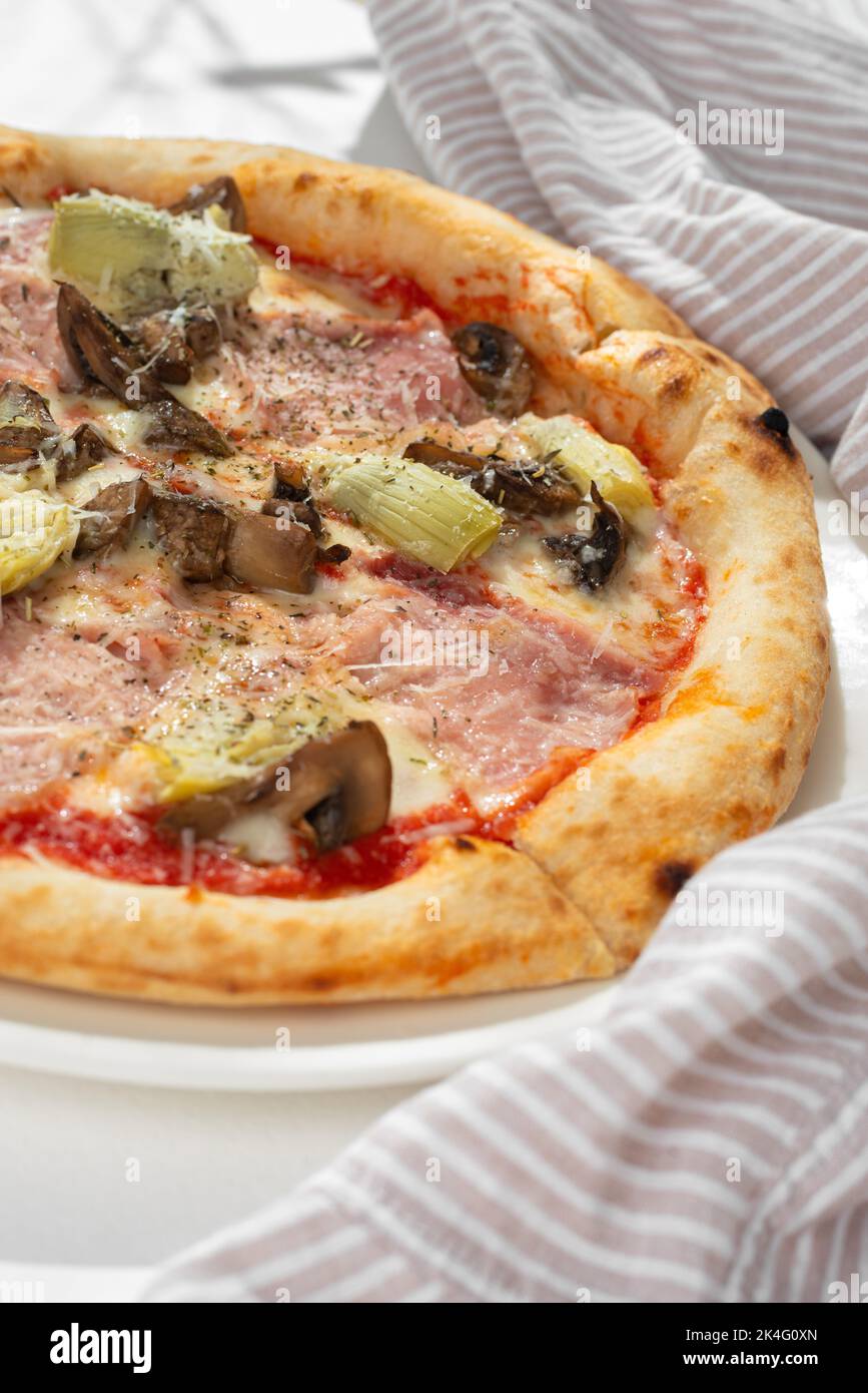 Pizza capricciosa with white mushrooms, ham, artichoke, tomatoes