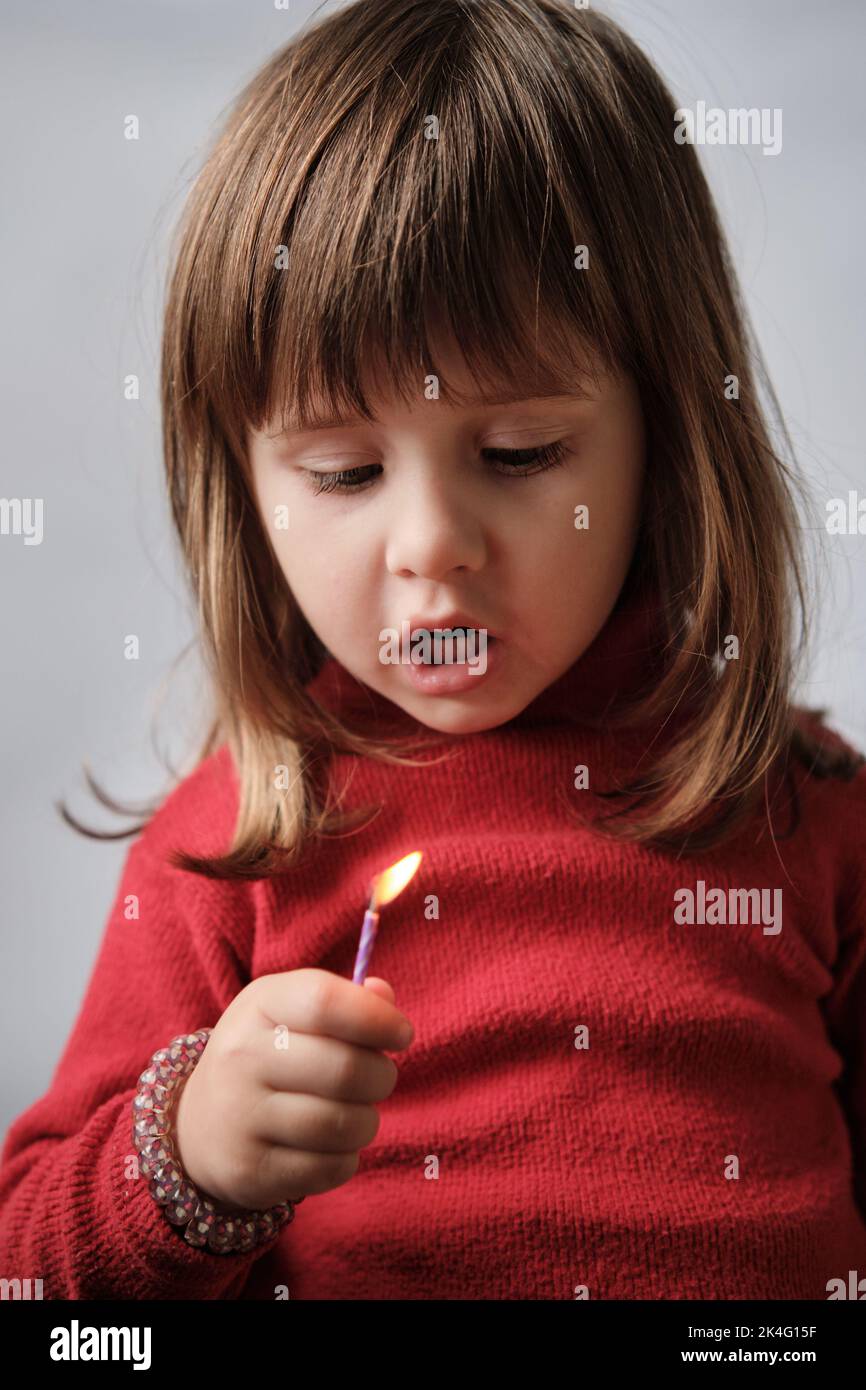 Portrait of little girl blowing out burning candle. Child holding