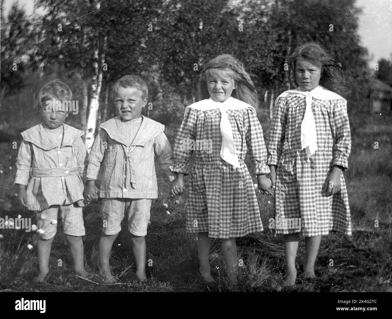 Group picture of four children. Two boys in the same striped costumes with sailor collar and short pants. Two girls in similar checkered dresses with white collars. Nordic Stock Photo