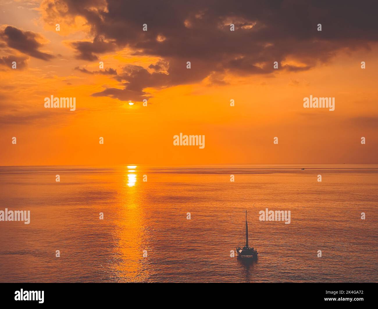 Bright orange sunset sky over sea and yacht boat. Dramatic cloudy sky, golden hour. Beautiful romantic scenic image of stunning seascape. Nature background. Summer vacation, travel, adventure concept Stock Photo