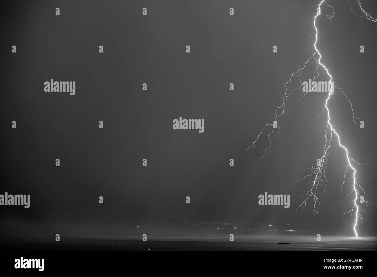 A black and white of a lightning and storm clouds over the sea and the ...