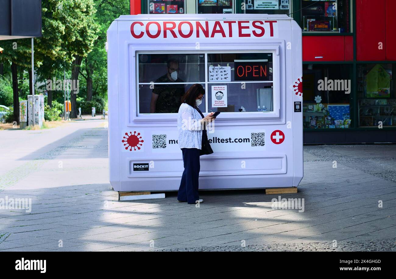 Berlin, Germany. 26th June, 2022. 26.06.2022, Berlin. A woman with a mask in front of her face stands in front of a Corona test center in Steglitz to be tested. While doing so, she looks at her smartphone. Credit: Wolfram Steinberg/dpa **Use in full format only**. Credit: Wolfram Steinberg/dpa/Alamy Live News Stock Photo