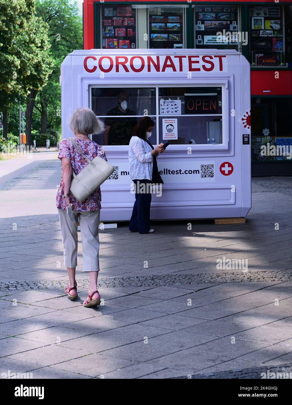 Berlin, Germany. 26th June, 2022. 26.06.2022, Berlin. A woman with a mask in front of her face stands in front of a Corona test center in Steglitz to be tested. While doing so, she looks at her smartphone. Credit: Wolfram Steinberg/dpa **Use in full format only**. Credit: Wolfram Steinberg/dpa/Alamy Live News Stock Photo