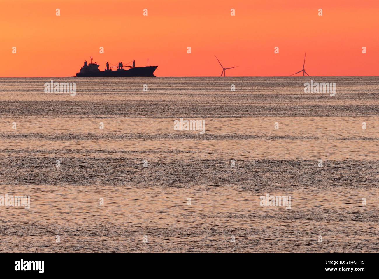 Dranske, Germany. 28th June, 2021. 28.06.2021, Dranske on Ruegen. Windmills of an offshore wind farm for power generation can be seen in the light of the setting sun in the Baltic Sea from the shore near Dranske on Ruegen. A cargo ship sails alongside. Credit: Wolfram Steinberg/dpa Credit: Wolfram Steinberg/dpa/Alamy Live News Stock Photo