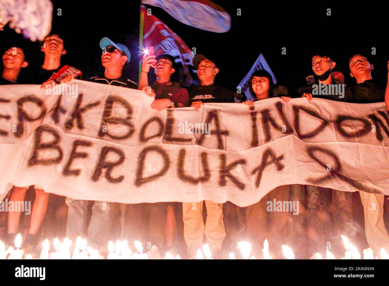 Indonesian football fans hold a banner and light candles in memory of