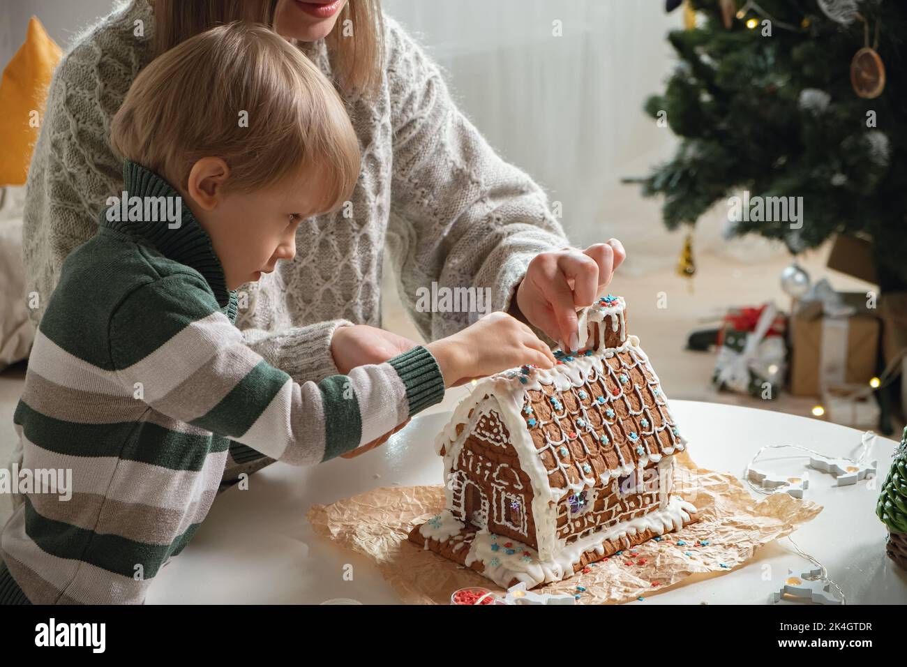 Little boy with mother decorating christmas gingerbread house together, family activities and traditions on Christmas and New Year's Eve Stock Photo