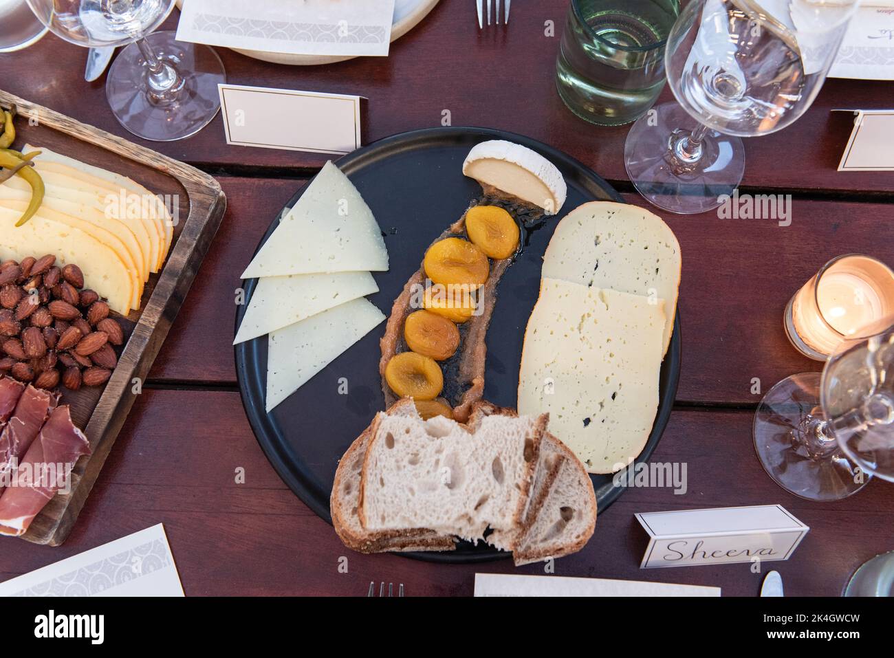 Party guests are privy to eat the charcuterie board featuring dried apricots over apple sauce, goat cheese, sourdough bread, and brie for an appetizer Stock Photo