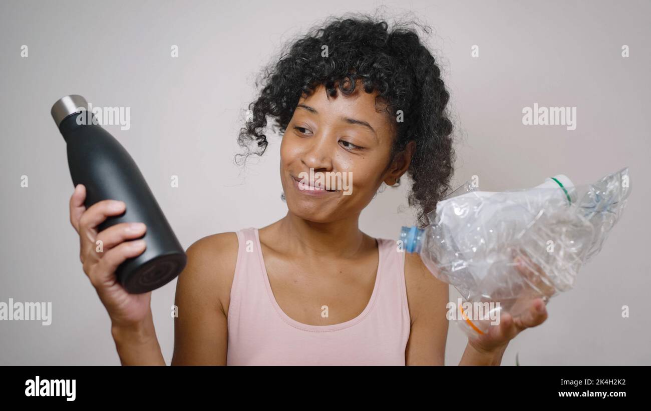 African American woman compares plastic and organic bottles standing on