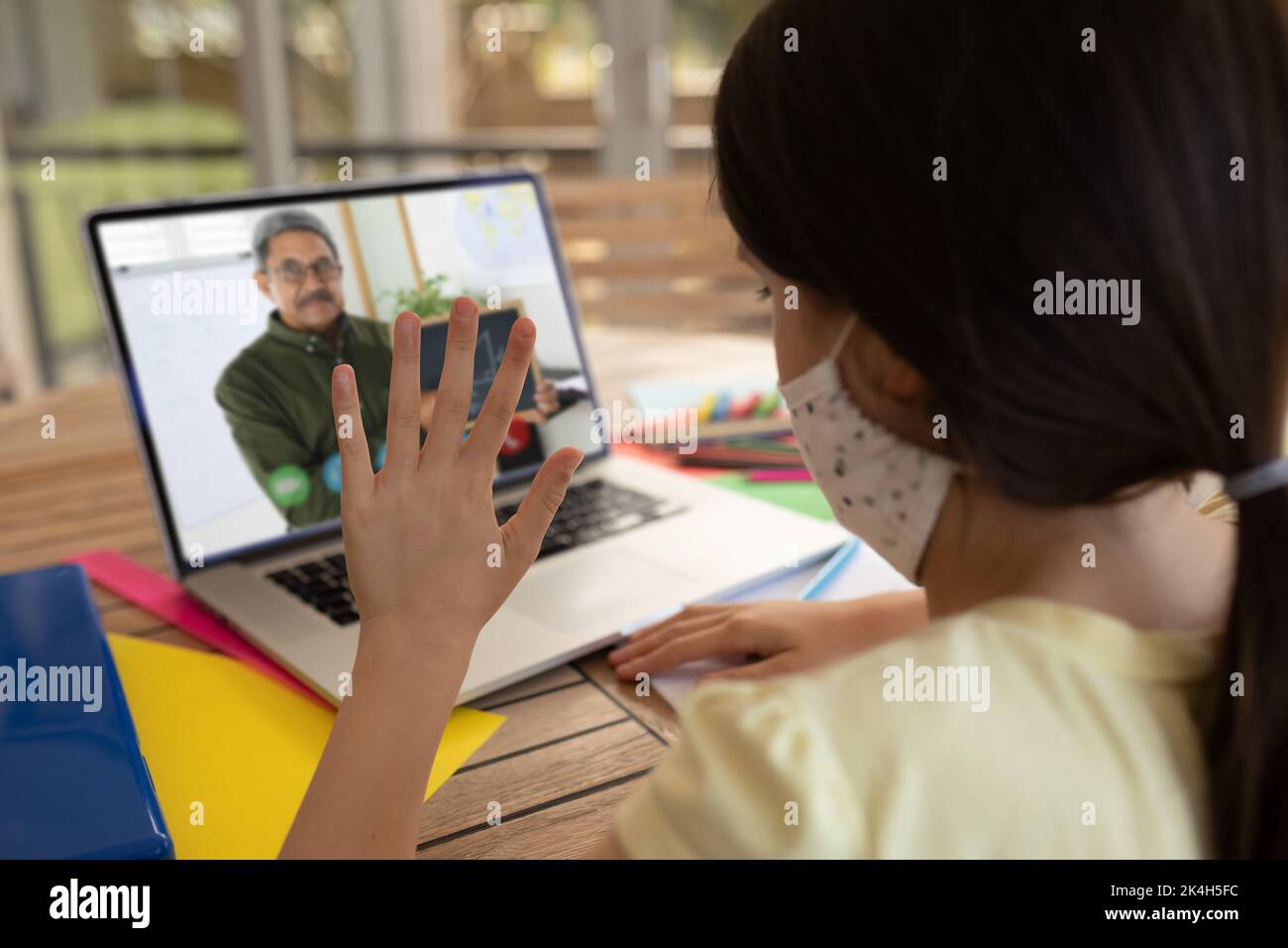 Female student wearing face mask having a video call with male teacher ...