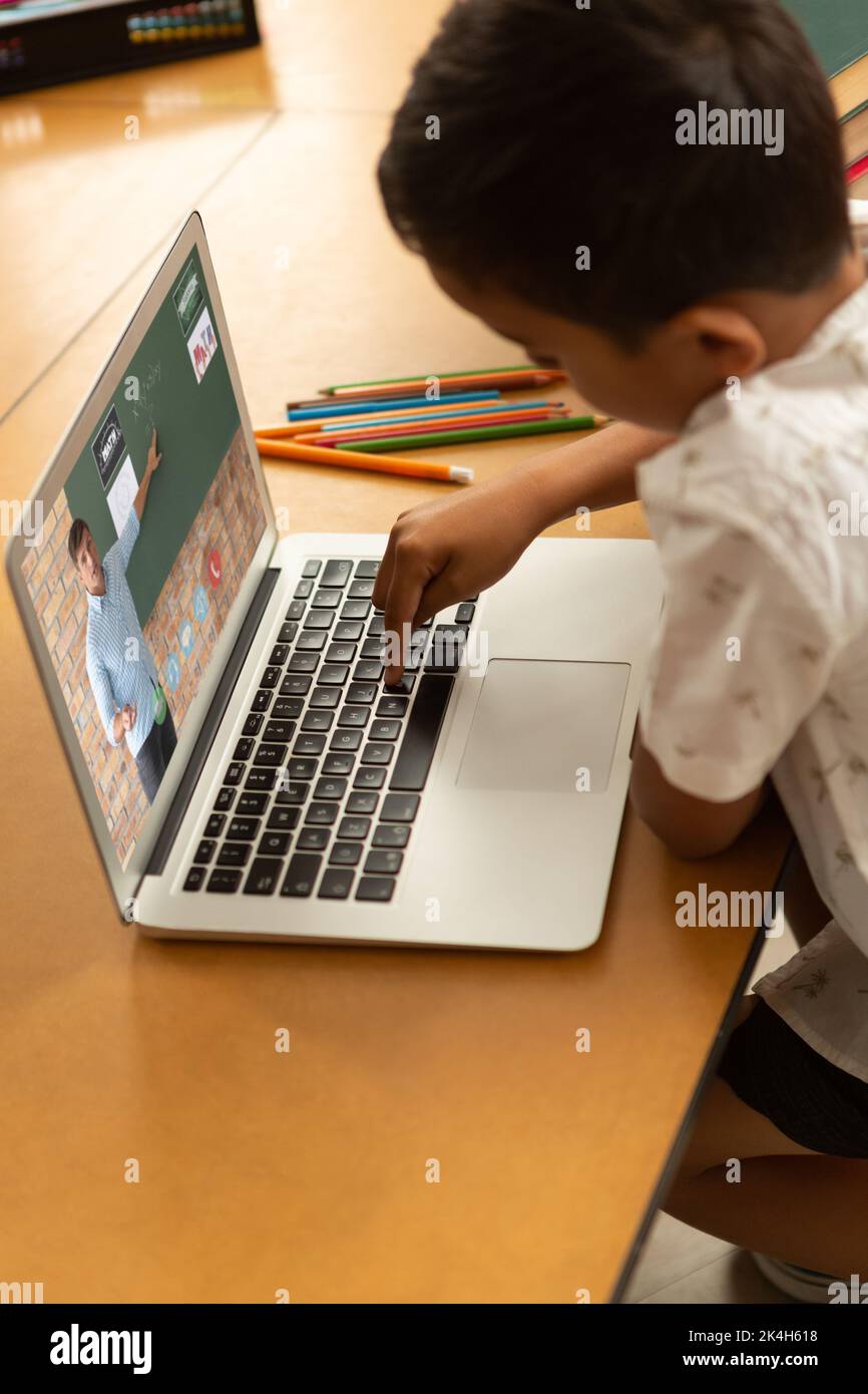Male student having a video call with male teacher on laptop at school ...