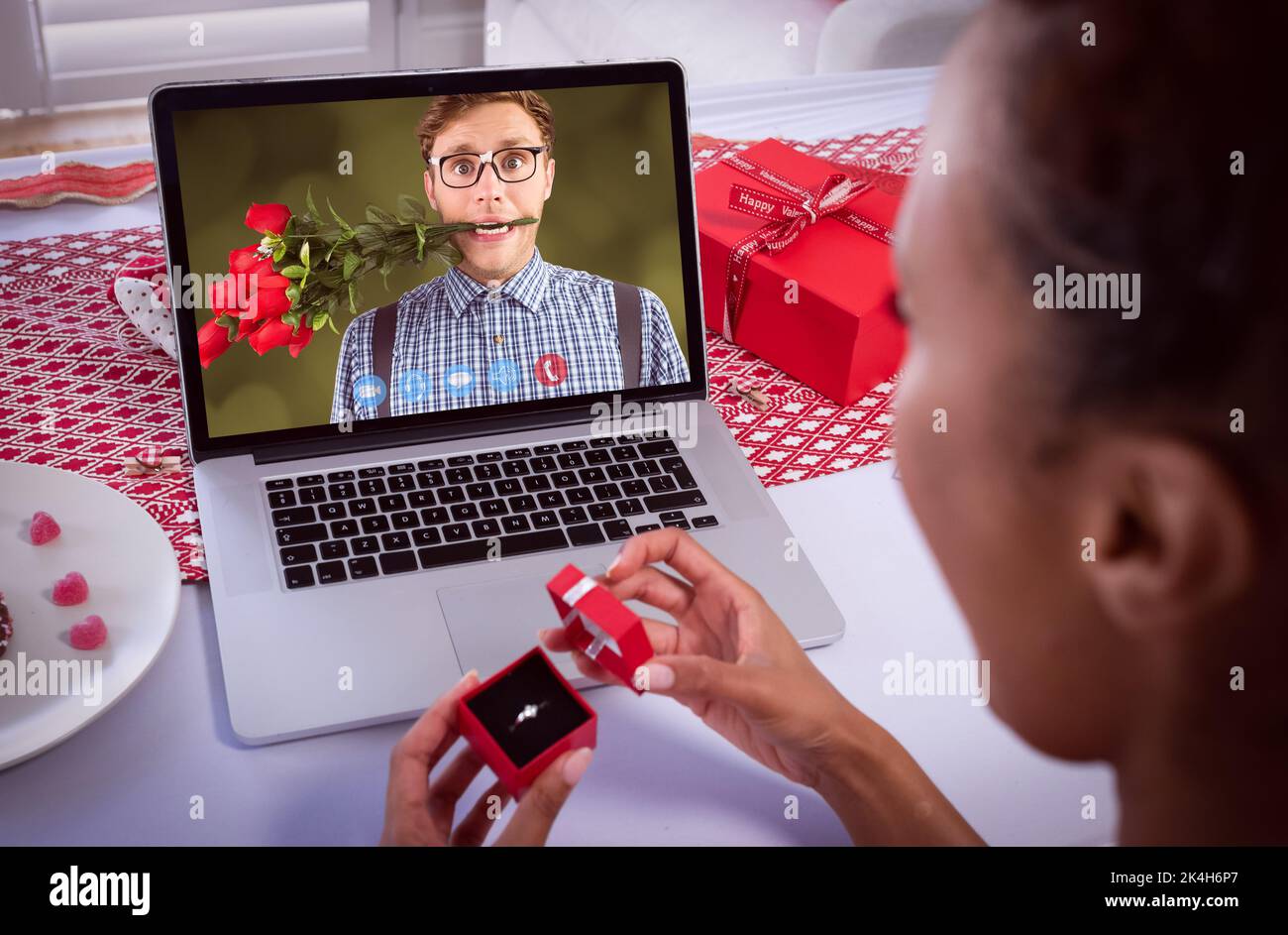 Diverse couple making valentines date video call man on screen with flowers between teeth and woman holding ring. online valentines day during quarant Stock Photo
