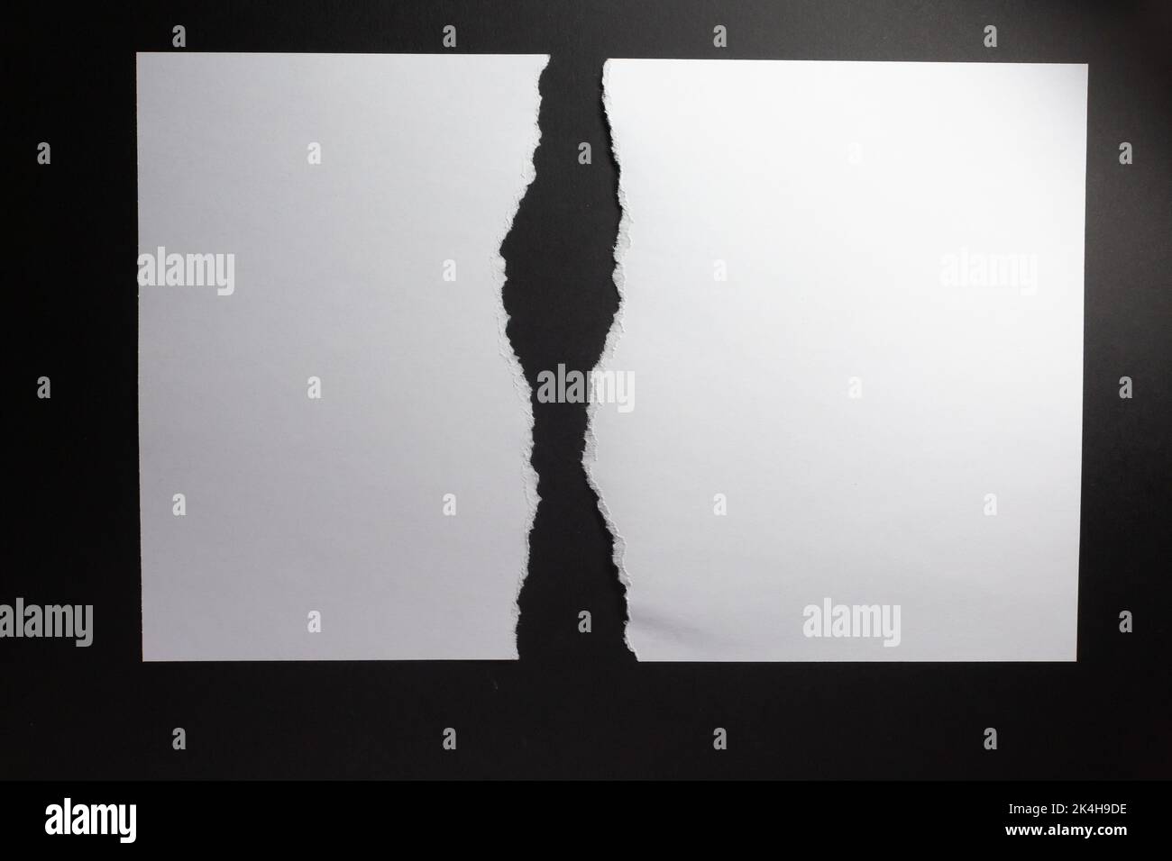 Two vertical sheets of white paper with torn edges facing, on black ...
