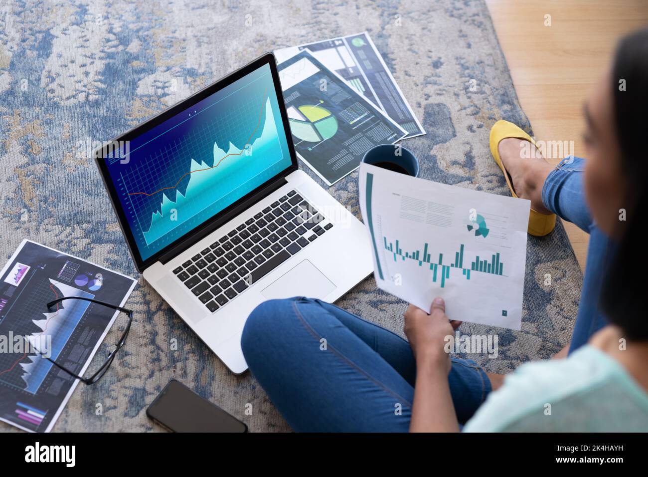 Woman Using Computer And Digital Technology Biracial woman sitting on floor, using computer with statistical data ...