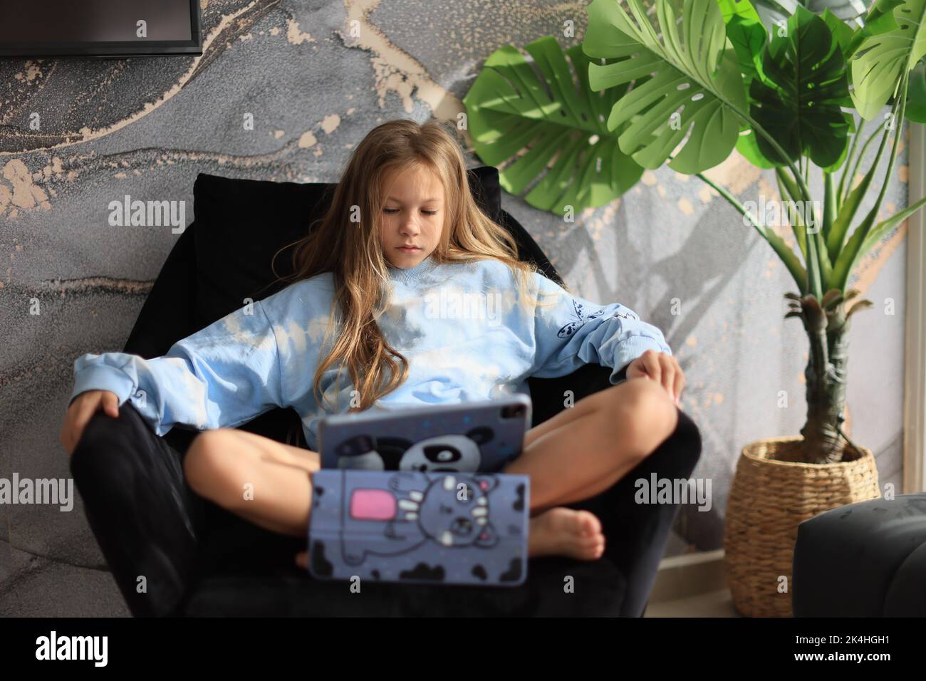 Curious cute kid girl using digital tablet technology device sitting on sofa alone Stock Photo
