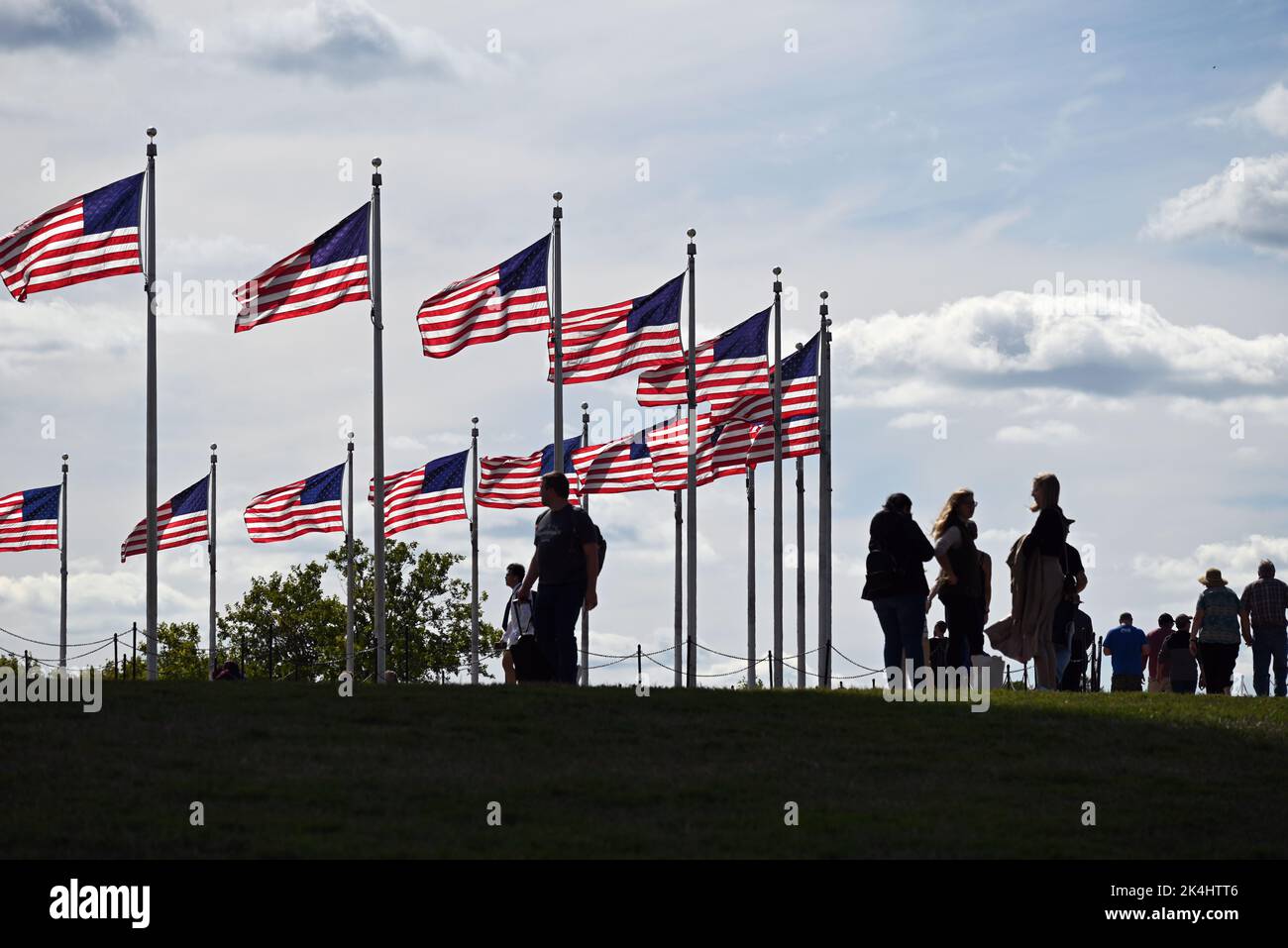 Tourists are silhouetted as they walk past the flags that encircle the base of the Washington Monument in Washington, DC. Stock Photo