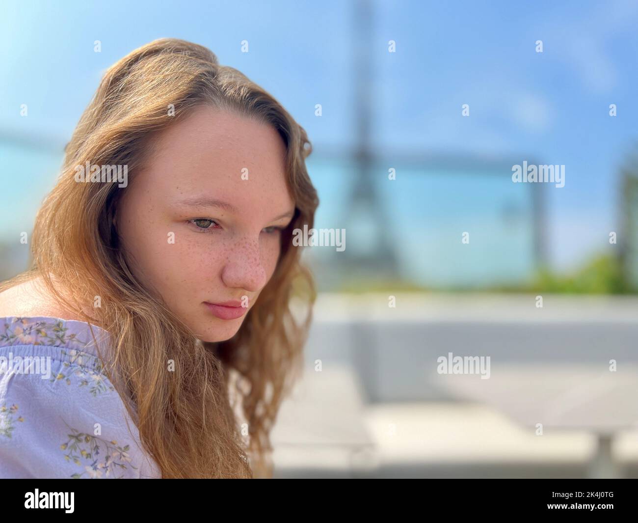 tender face of a girl with freckles close-up she has blond hair and bright eyes She looks and can be used for any advertisement there is a place for text. Eiffel Tower in the background Stock Photo