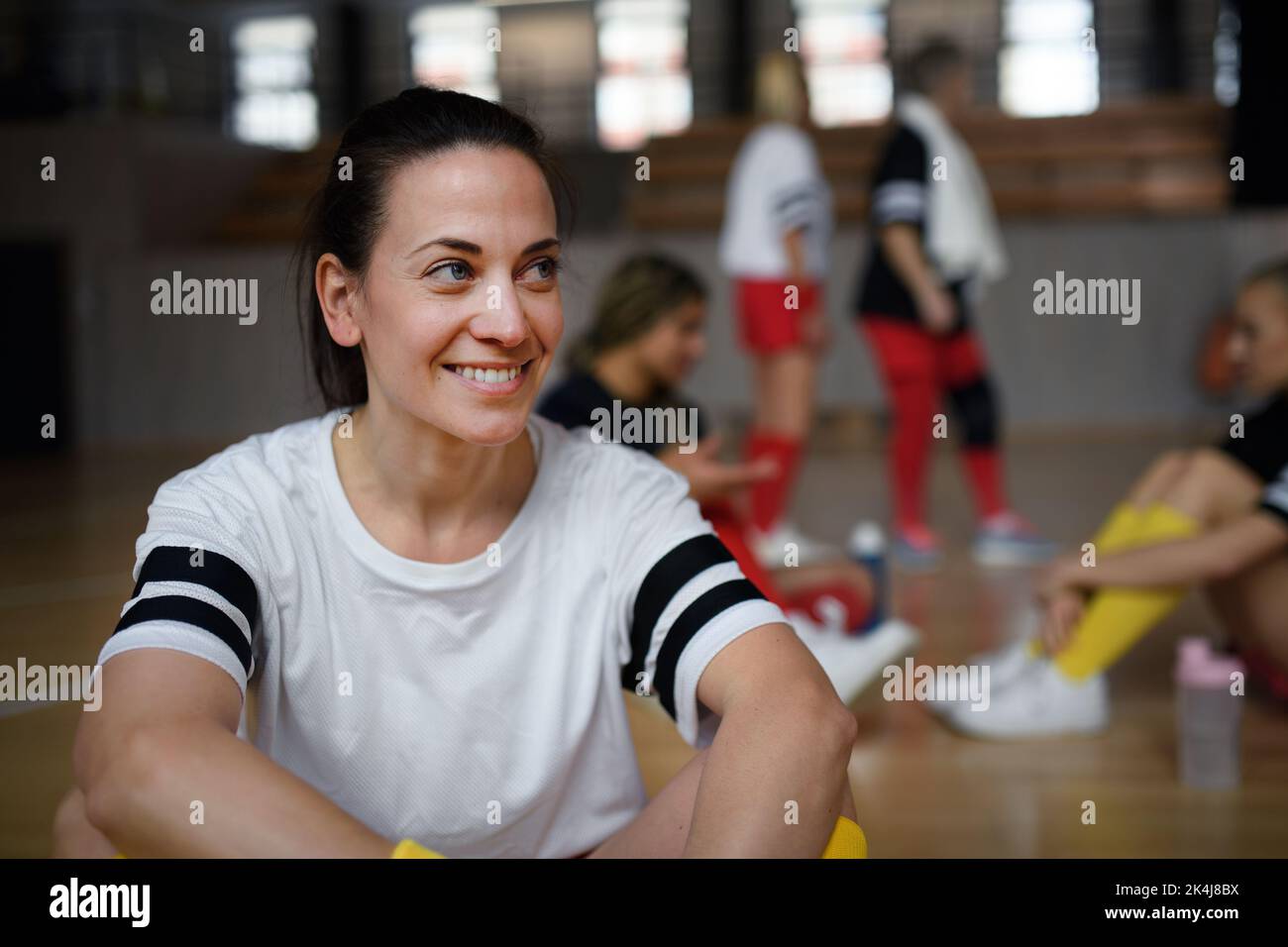 Group of young and old women, sports team players in gym sitting and resting after match. Stock Photo