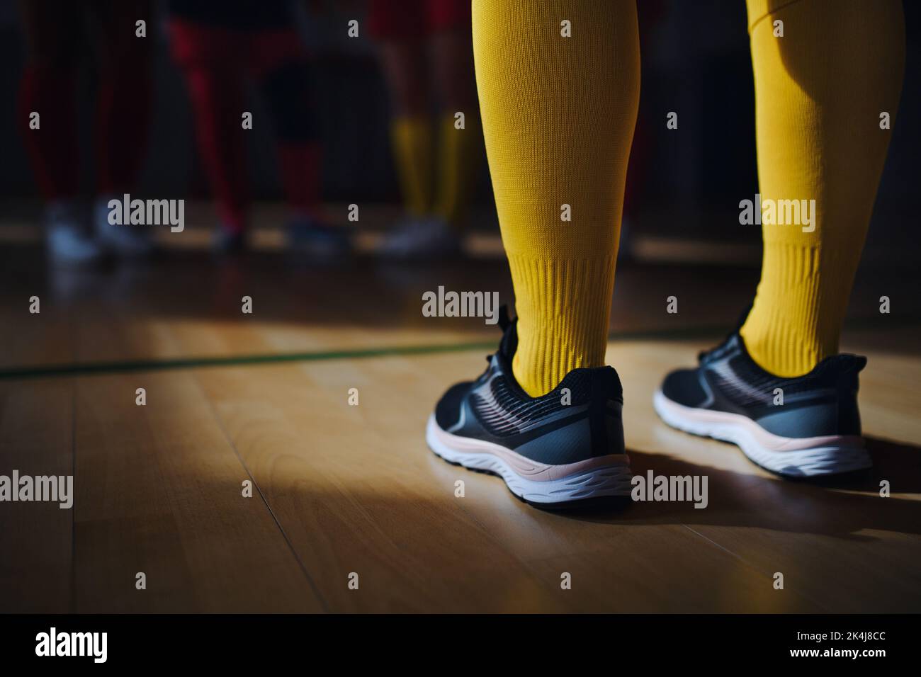 Close up of womans legs in knee socks and trainers in front of floorball mach in gym. Stock Photo