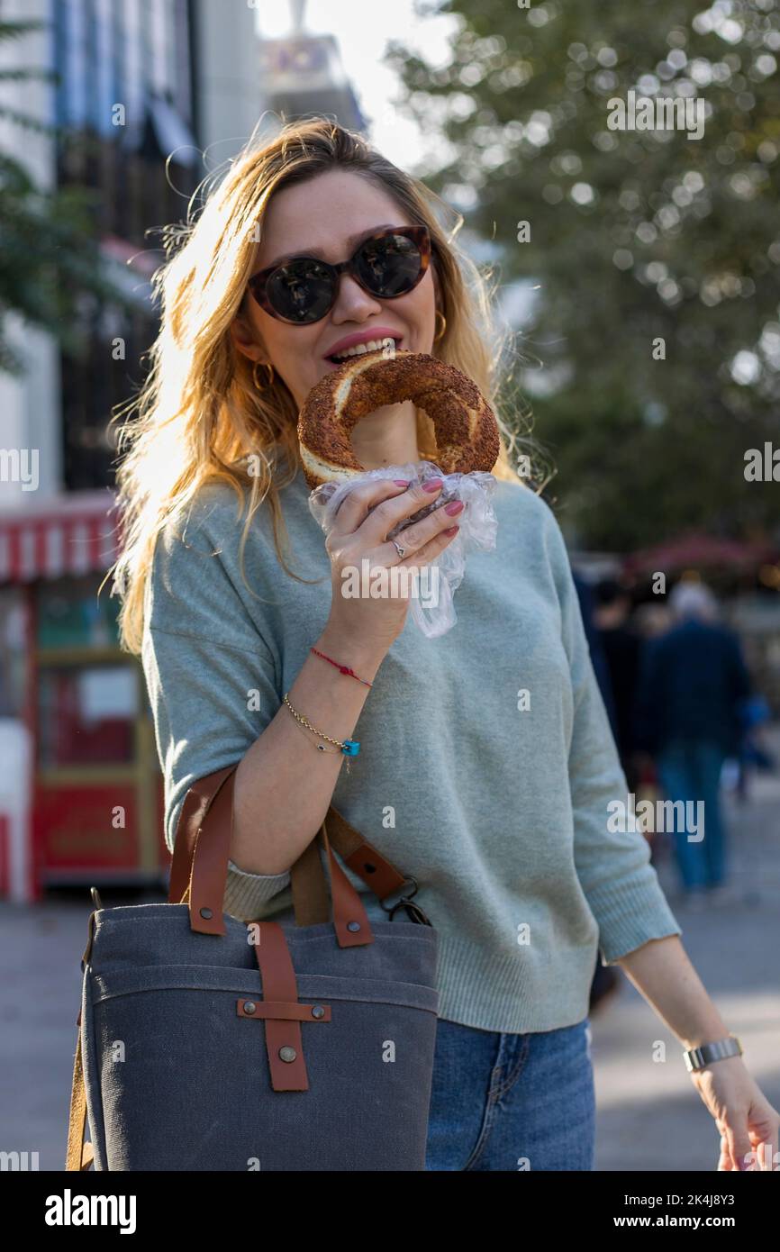 Blonde woman eating traditional Turkish bread bagel on the street. Istanbul Turkey Stock Photo