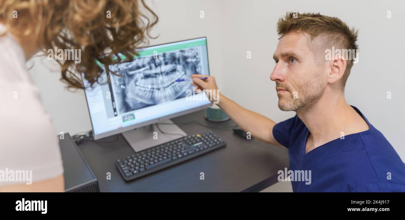 Young dentist showing x-ray scan at computer to patient. Stock Photo