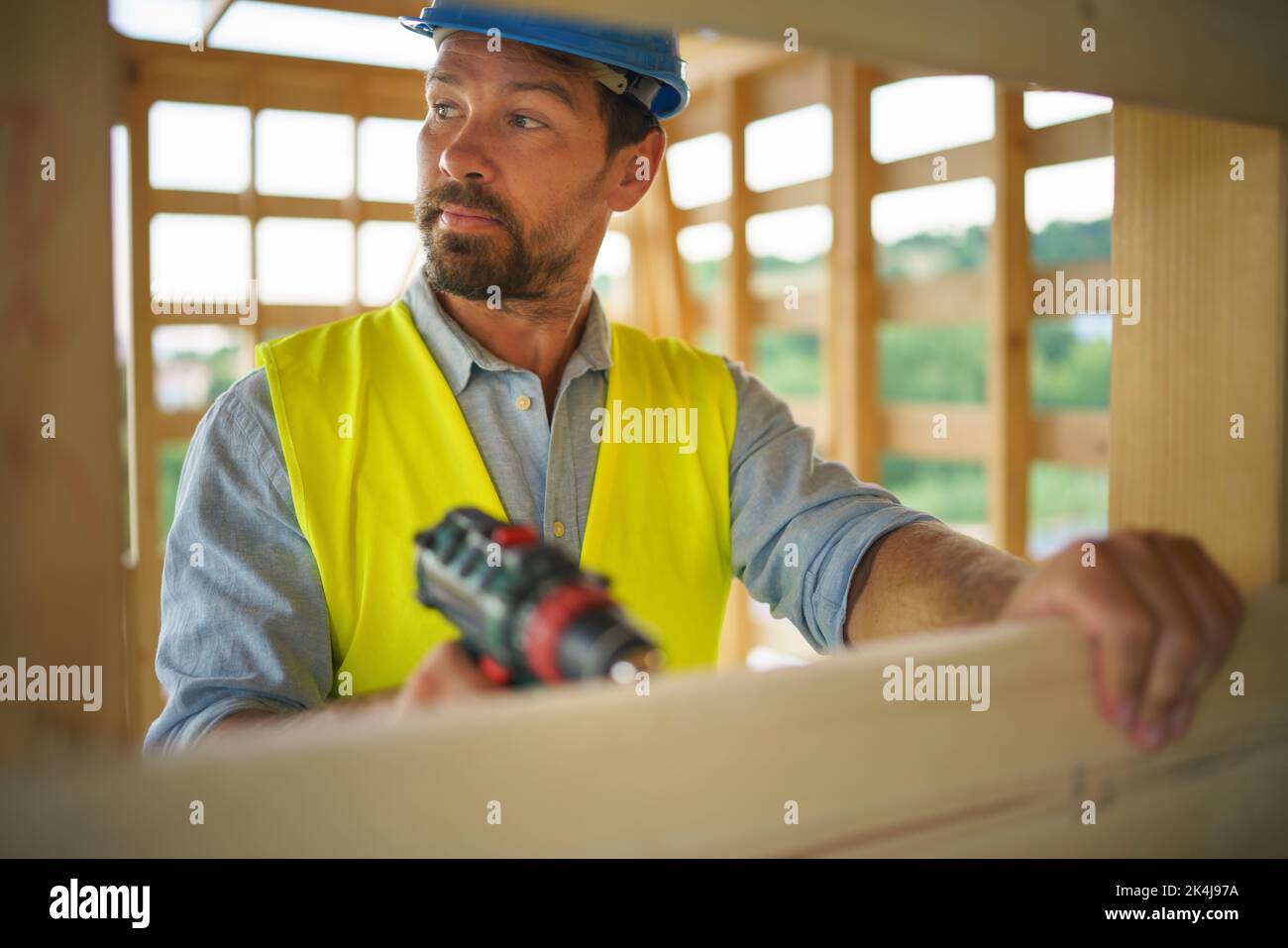 Construction worker working with electric screwdriver on wooden frame, diy eco-friendly homes concept. Stock Photo