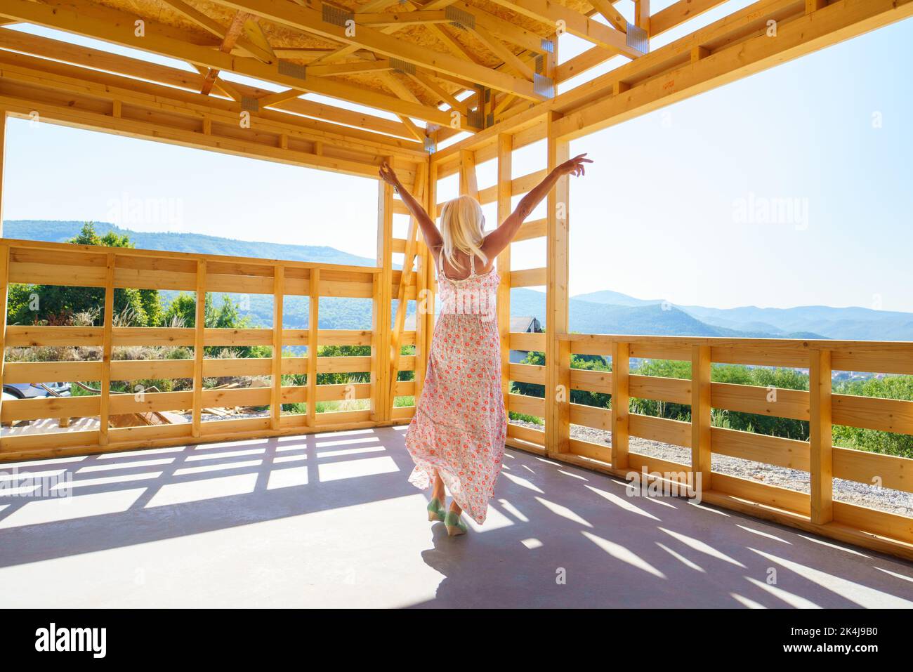 Excited senior woman inside of her new unfinished ecological wooden house. Stock Photo