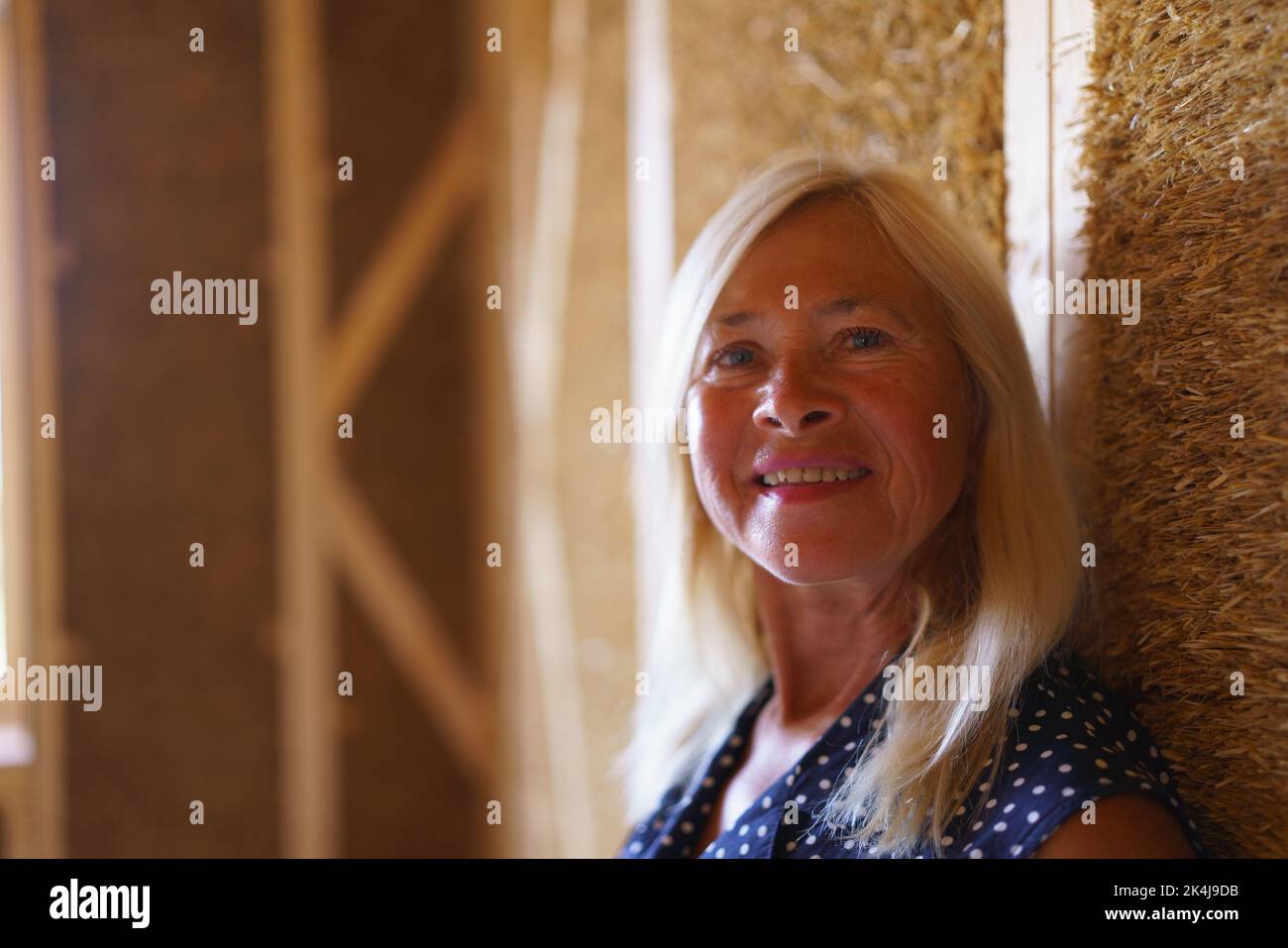 Portrait of happy senior woman inside of her new unfinished ecological wooden house. Stock Photo