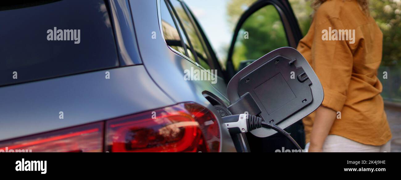 Woman waiting while electric car charging, close-up. Stock Photo