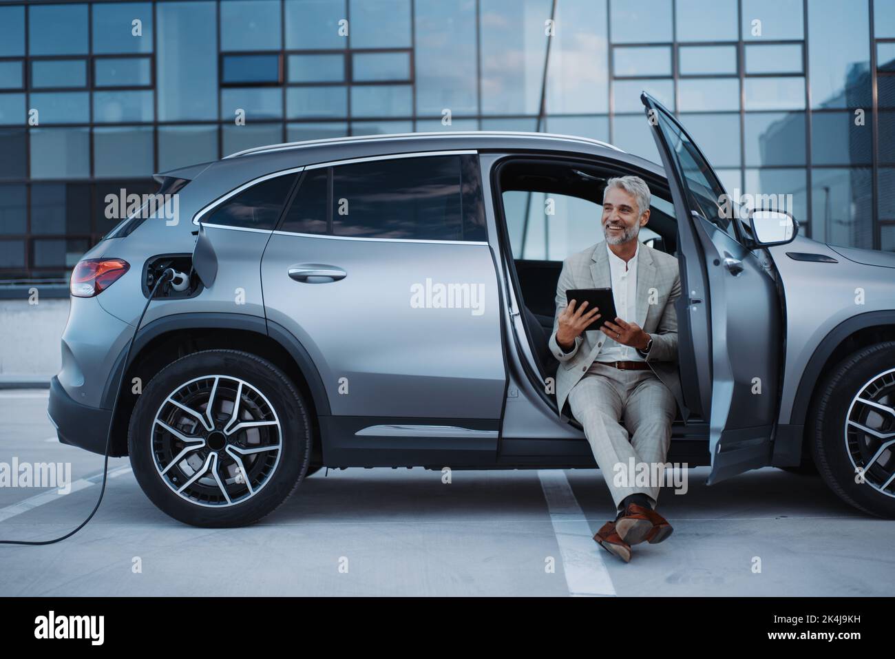 Businessman using tablet while charging car at electric vehicle