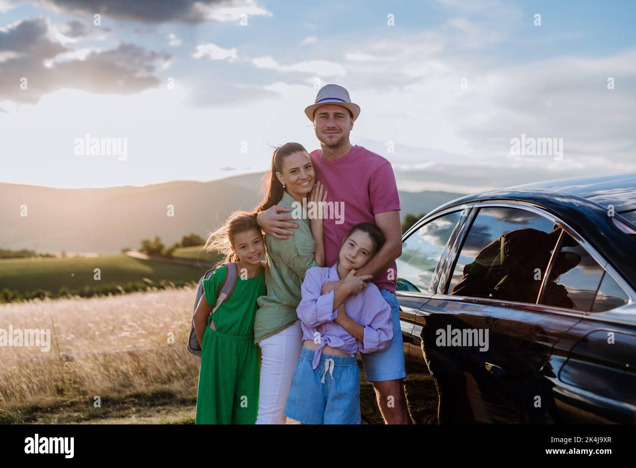 Happy family on car trip having break in nature, next their electric car. Stock Photo