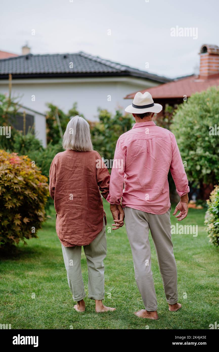 Rear view of senior couple posing together in their garden, holding each other hands. Stock Photo