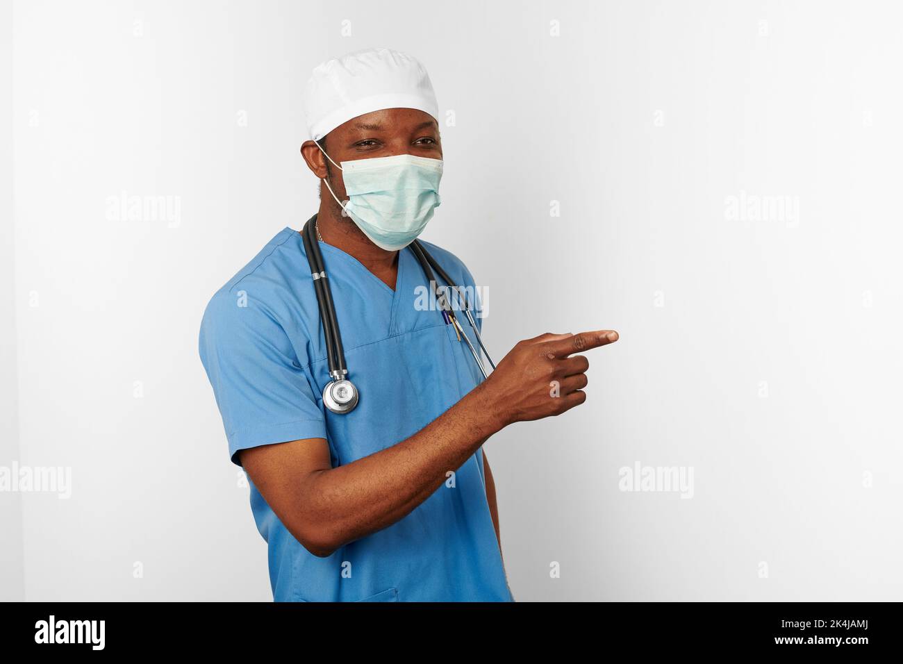 Black surgeon doctor man in blue coat white cap and surgeon mask pointing  finger to right isolated on white background. Focused adult black african  am Stock Photo - Alamy