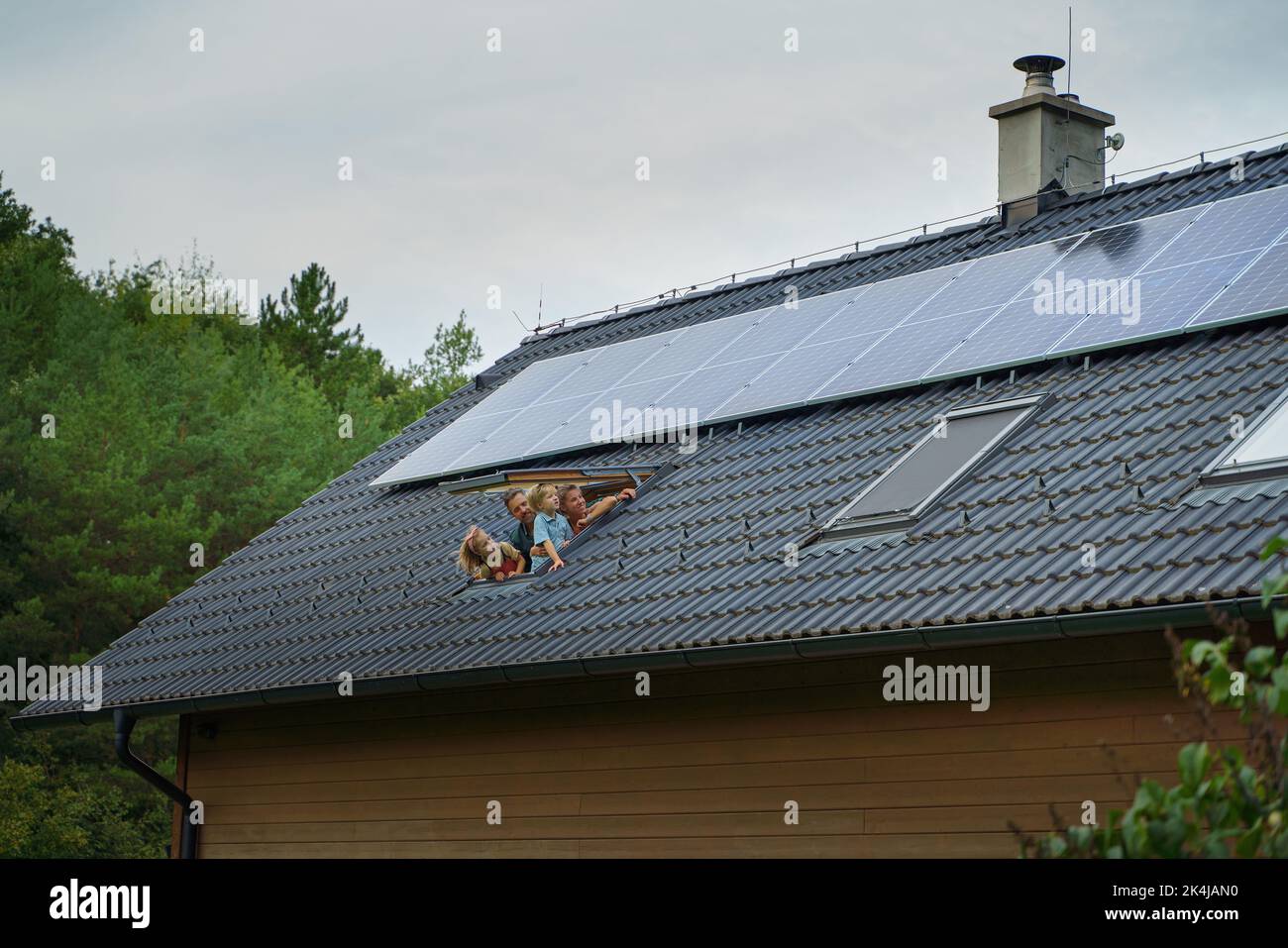 Happy family looking out from skylight window in their new house with solar panels on the roof. Alternative energy, saving resources and sustainable Stock Photo