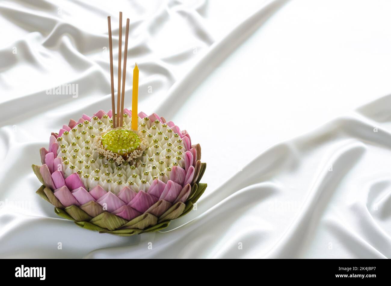 Pink lotus petal krathong for Thailand Loy Krathong festival decorates with its pollen, crown flower, incense stick and candle on smooth and wavy whit Stock Photo