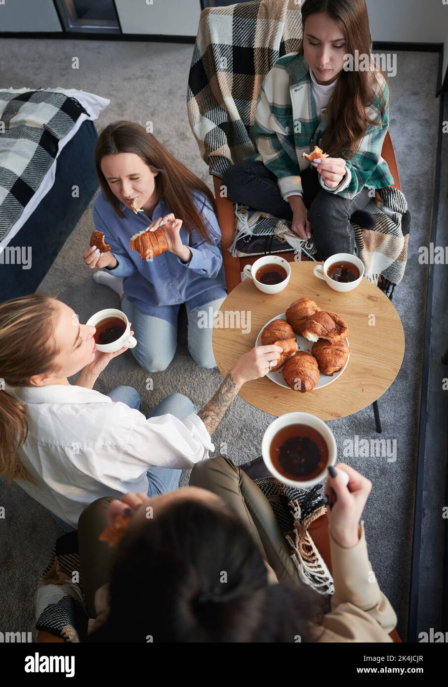 Young women enjoying winter weekends inside contemporary barn house. Four girls having fun and eating croissants and drinking hot tea. Stock Photo